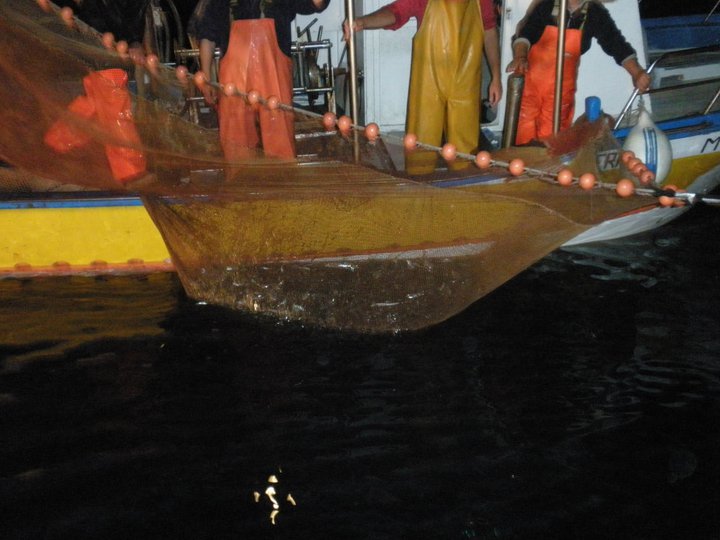 Barca da pesca con lampara accesa di notte — luce intensa sul mare scuro